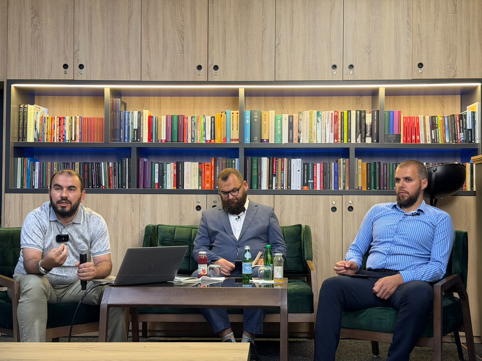 Tre folës në kolltukë para rafteve me libra gjatë një diskutimi